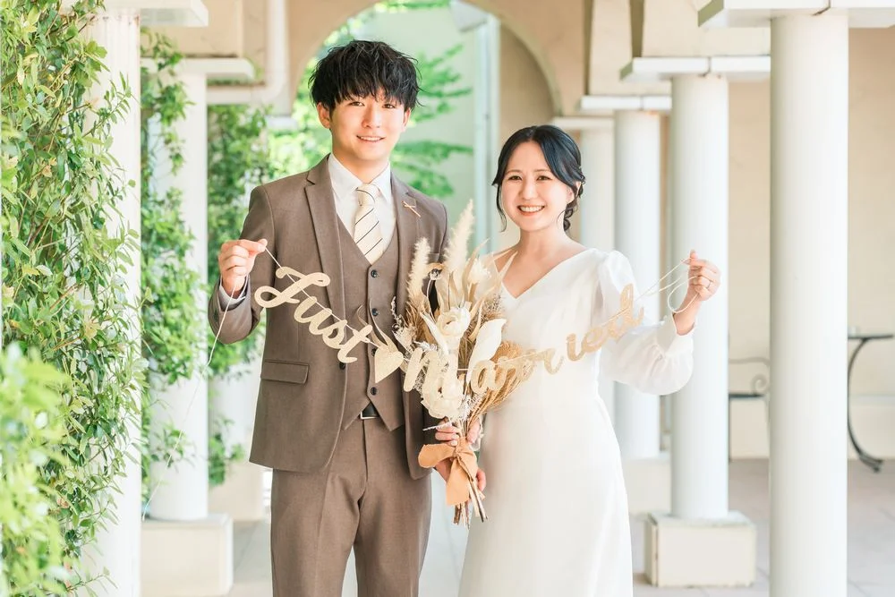 「Just Married」の飾りとブーケを手に、並んで微笑む男女